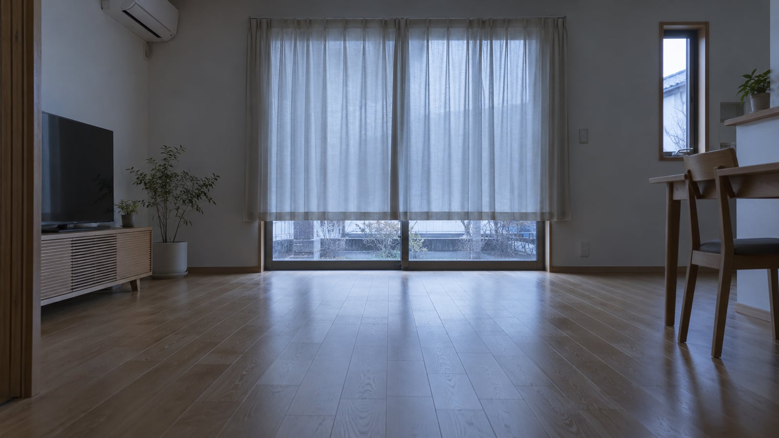 冬の朝、日差しの入らない一戸建てのリビングのフローリングと掃き出し窓